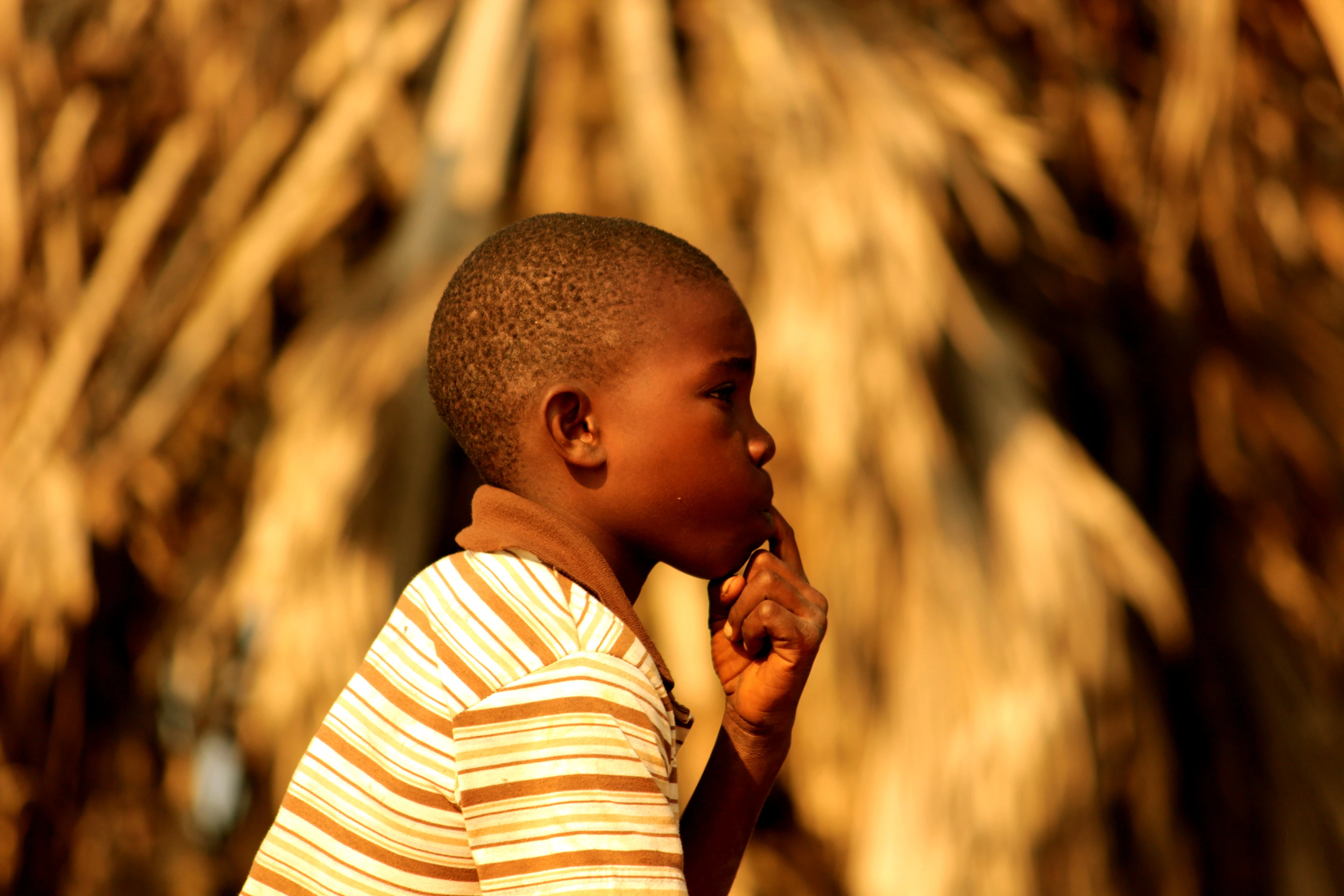 Boy in profile against straw roof, golden light