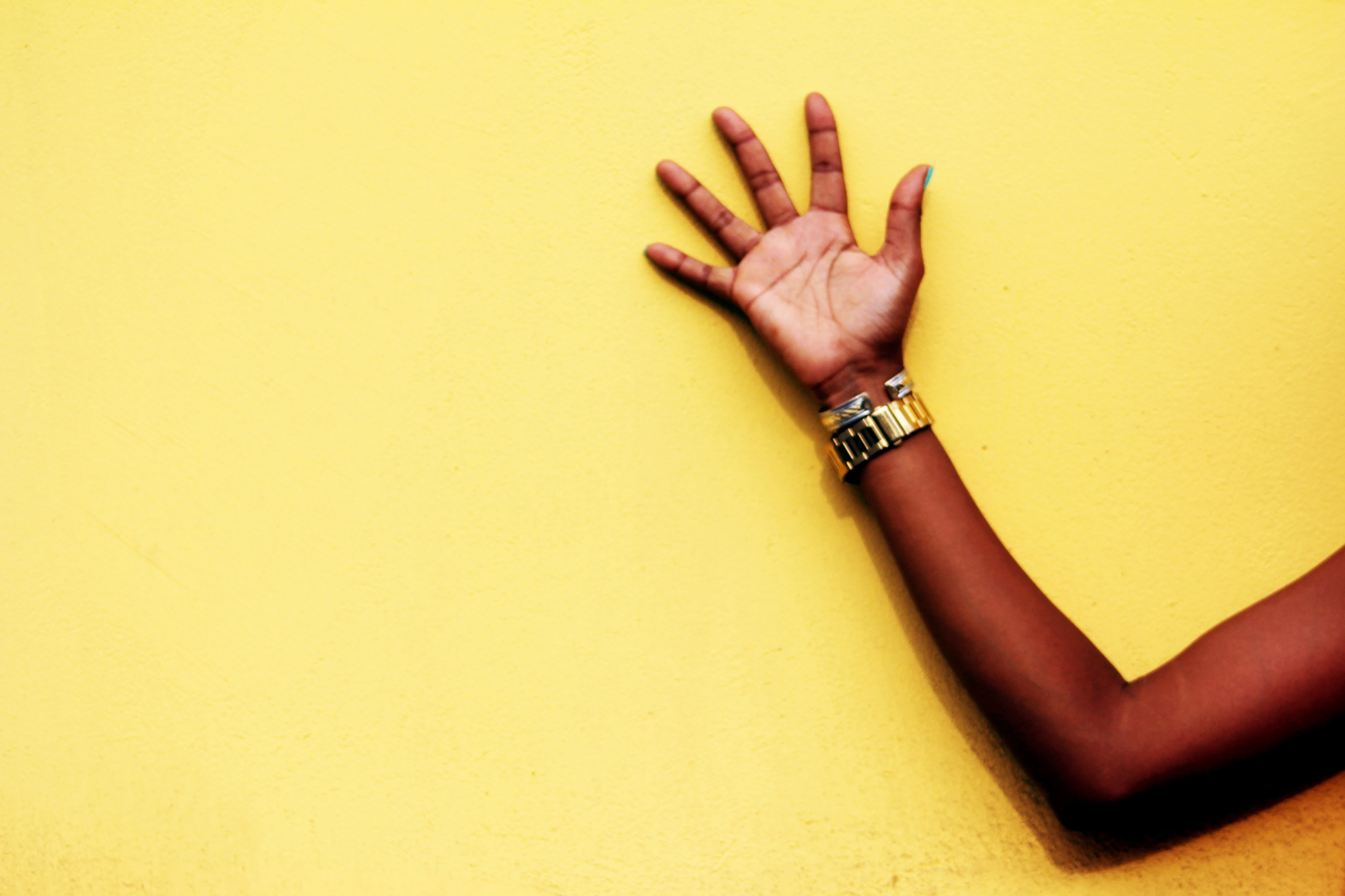Hand pressed against a yellow wall, bracelet and turquoise nails