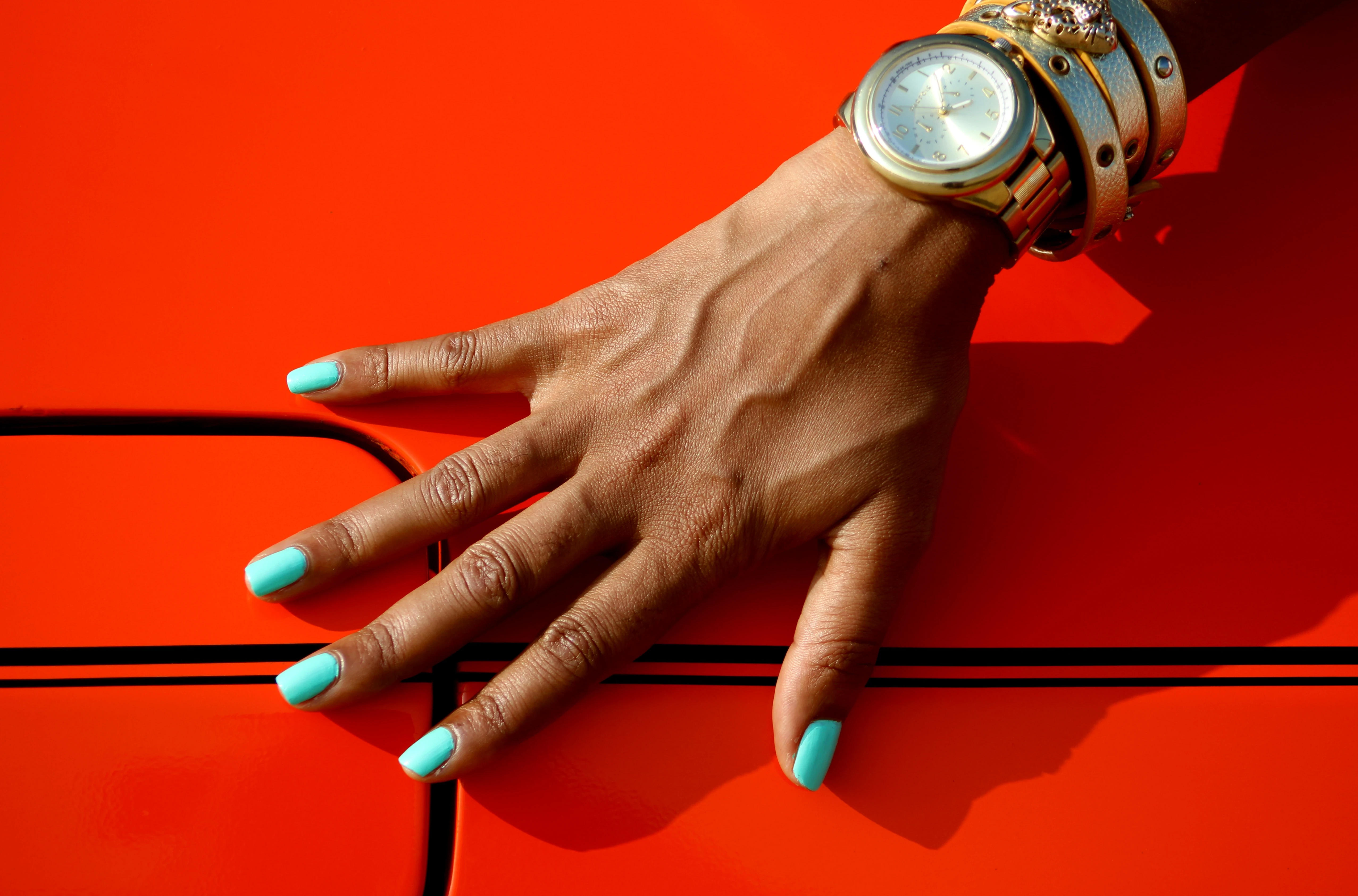 Hand with turquoise nails and gold watch on a red car
