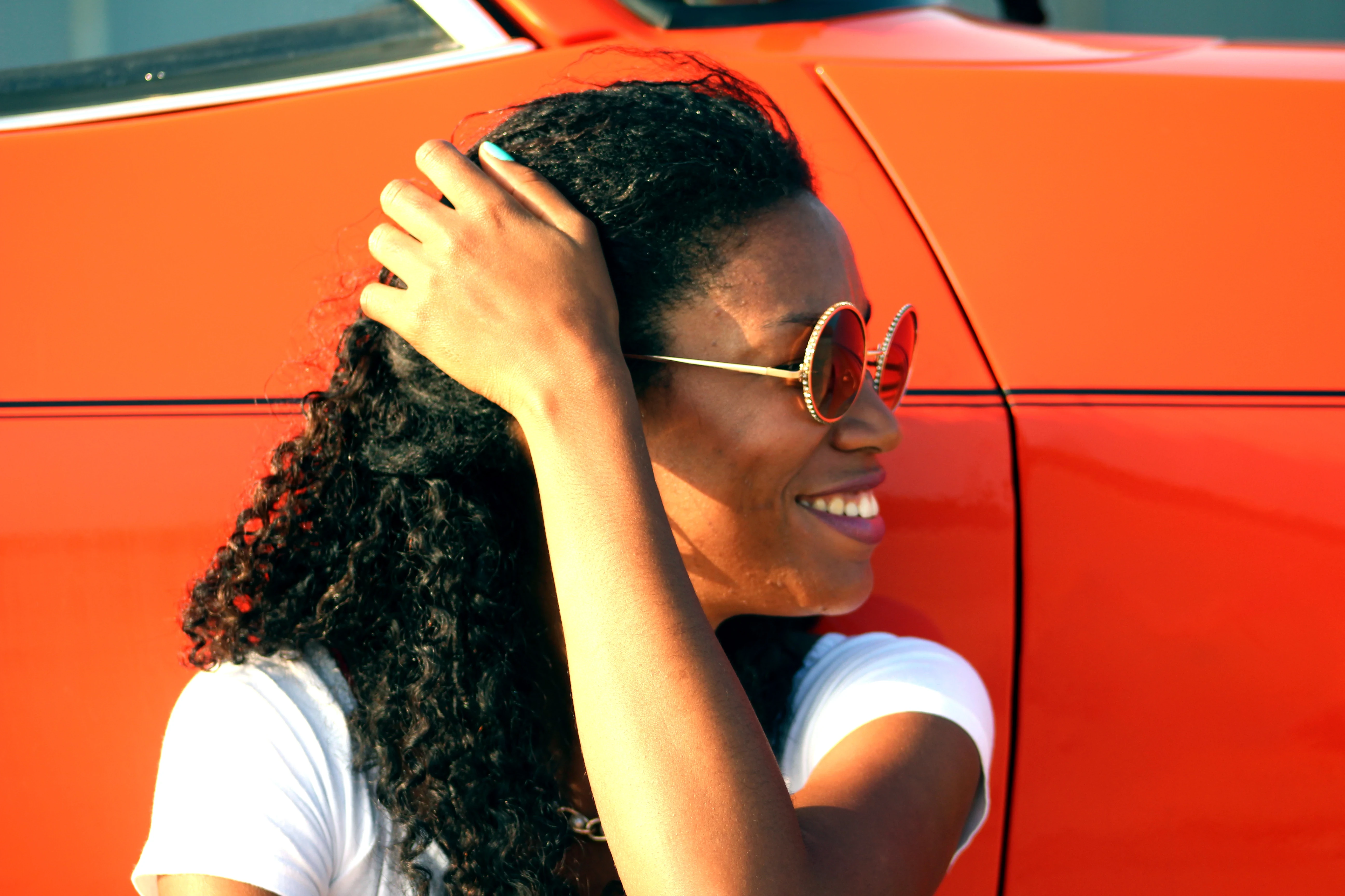 Woman smiling, leaning against a red vintage car